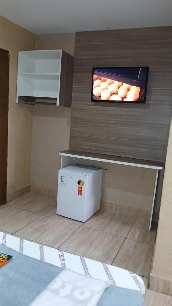 Habitación compacta con televisión de pantalla plana en la pared, un refrigerador blanco pequeño y un armario blanco.