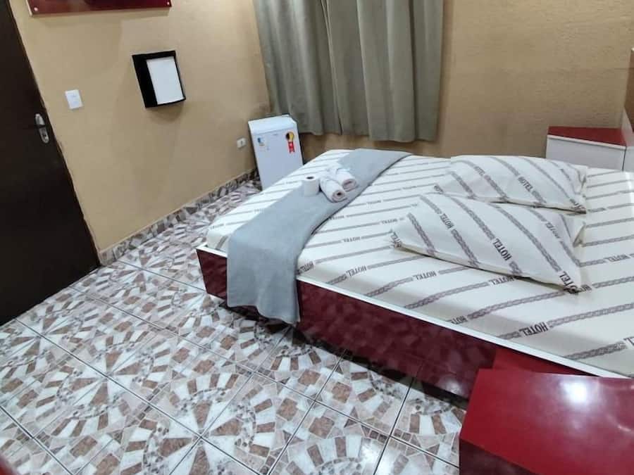 Ein Hotelzimmer mit Bett, Wandfernseher, kleinem Kühlschrank und einem Fenster mit Vorhängen.
