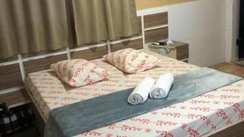 Una cama bien hecha con una colcha floral, una toalla enrollada y una mesita de noche con una lámpara.
