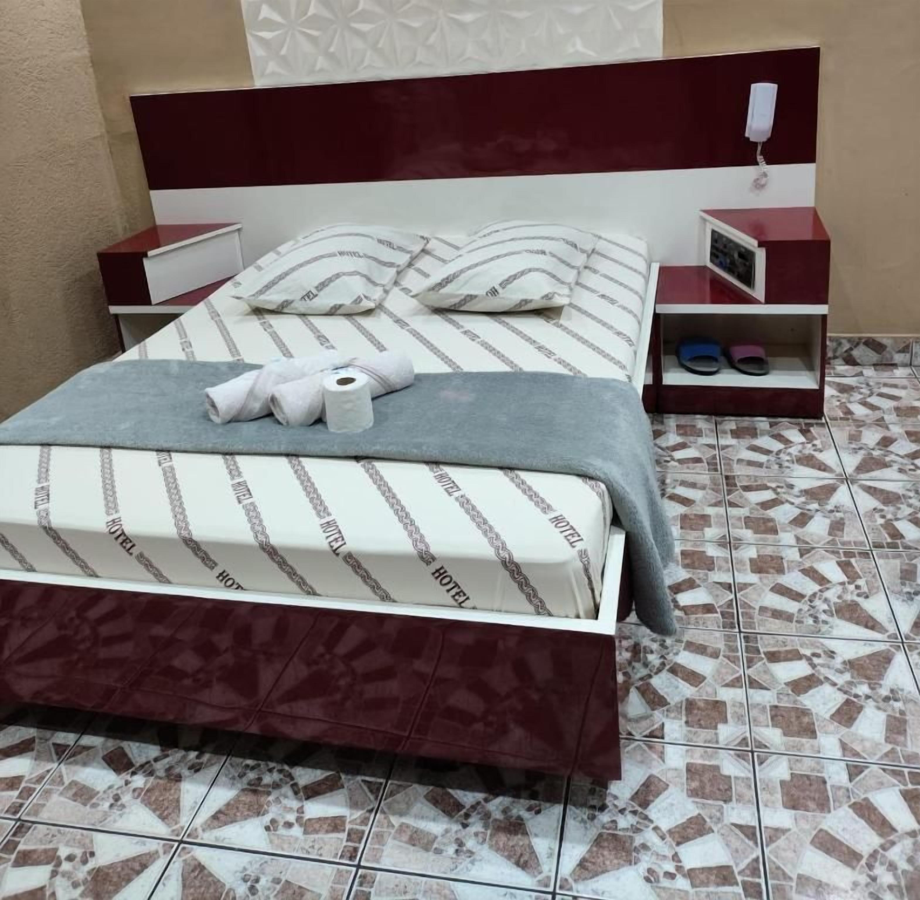A hotel room with a bed, a nightstand, a bedside table, and a wall-mounted telephone.