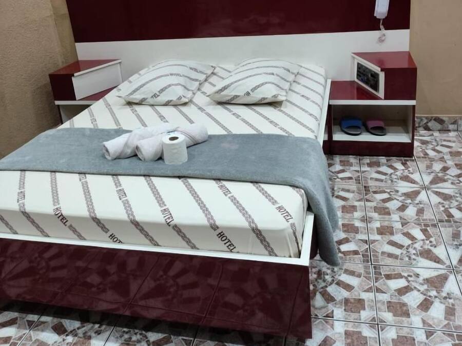 A hotel room with a bed, a nightstand, a bedside table, and a wall-mounted telephone.