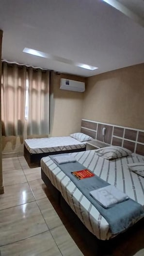 Habitación de hotel con dos camas, ventilador de techo, aire acondicionado y ventana con cortinas.