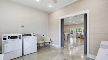 A laundry area with two washing machines, a chair, and a door leading to a living room.