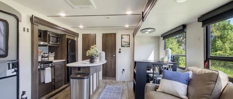 A compact RV interior with a kitchenette, a dining area, and a seating space with a view.