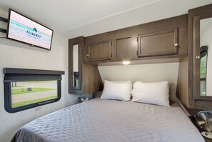 A bedroom with a bed, a television mounted on the wall, and a window with an 'EXIT' sign.