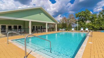 A swimming pool with a covered area, lounge chairs, and a fenced deck.