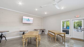 A conference room with wooden tables and chairs, a mounted TV screen, and an exit sign.