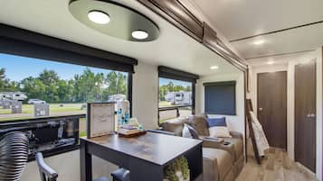 A modern RV interior with a dining area, seating, and a view of the outdoors.