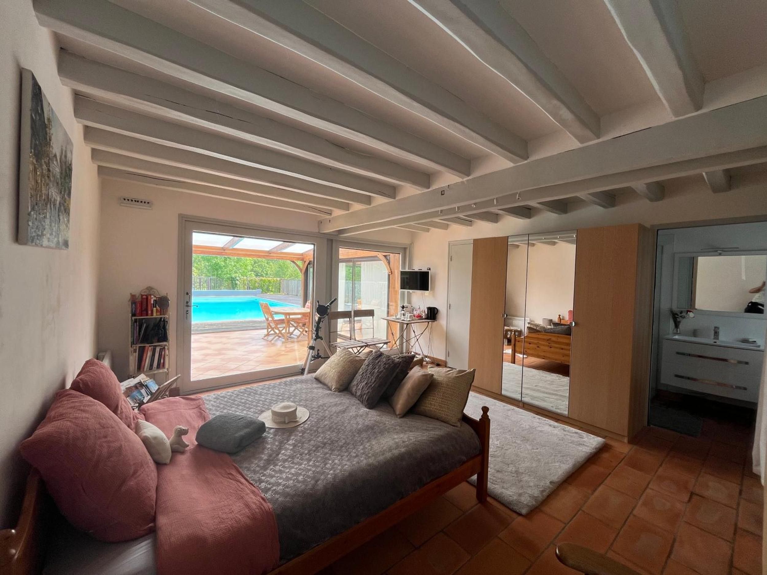 A bedroom with a bed, a sofa, a TV, and a view of an outdoor swimming pool.