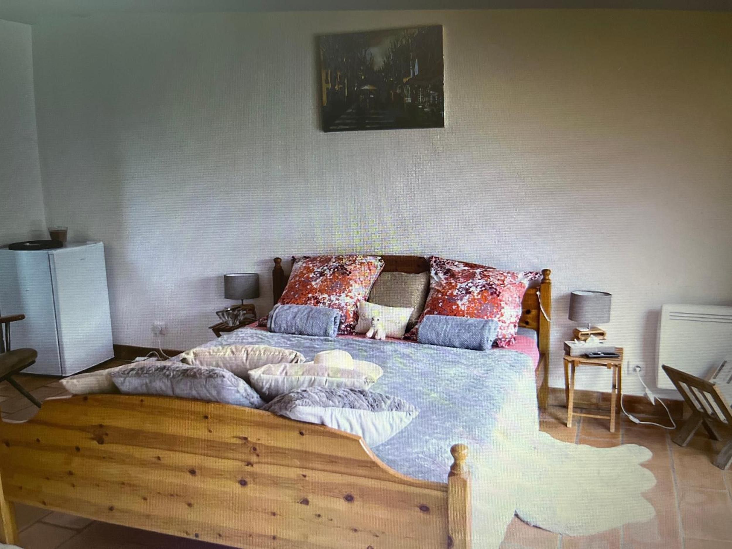 Une chambre à coucher avec un lit en bois, plusieurs oreillers, une table de chevet avec une lampe, un radiateur et un tableau accroché au mur.