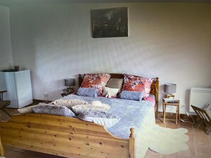 Ein Schlafzimmer mit einem hölzernen Bett, mehreren Kissen, einem Nachttisch mit Lampe, einem Heizkörper und einem Wandbild.
