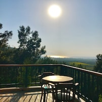 Un balcón con mesa y sillas, con vistas a un paisaje con árboles y una lejanía.
