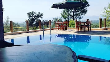A clear blue pool with a wooden table and chairs, surrounded by wooden pillars and a view of the landscape.