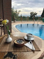 Escena junto a la piscina con una mesa, un jarrón blanco con una flor, una taza de café y un bol de postre.