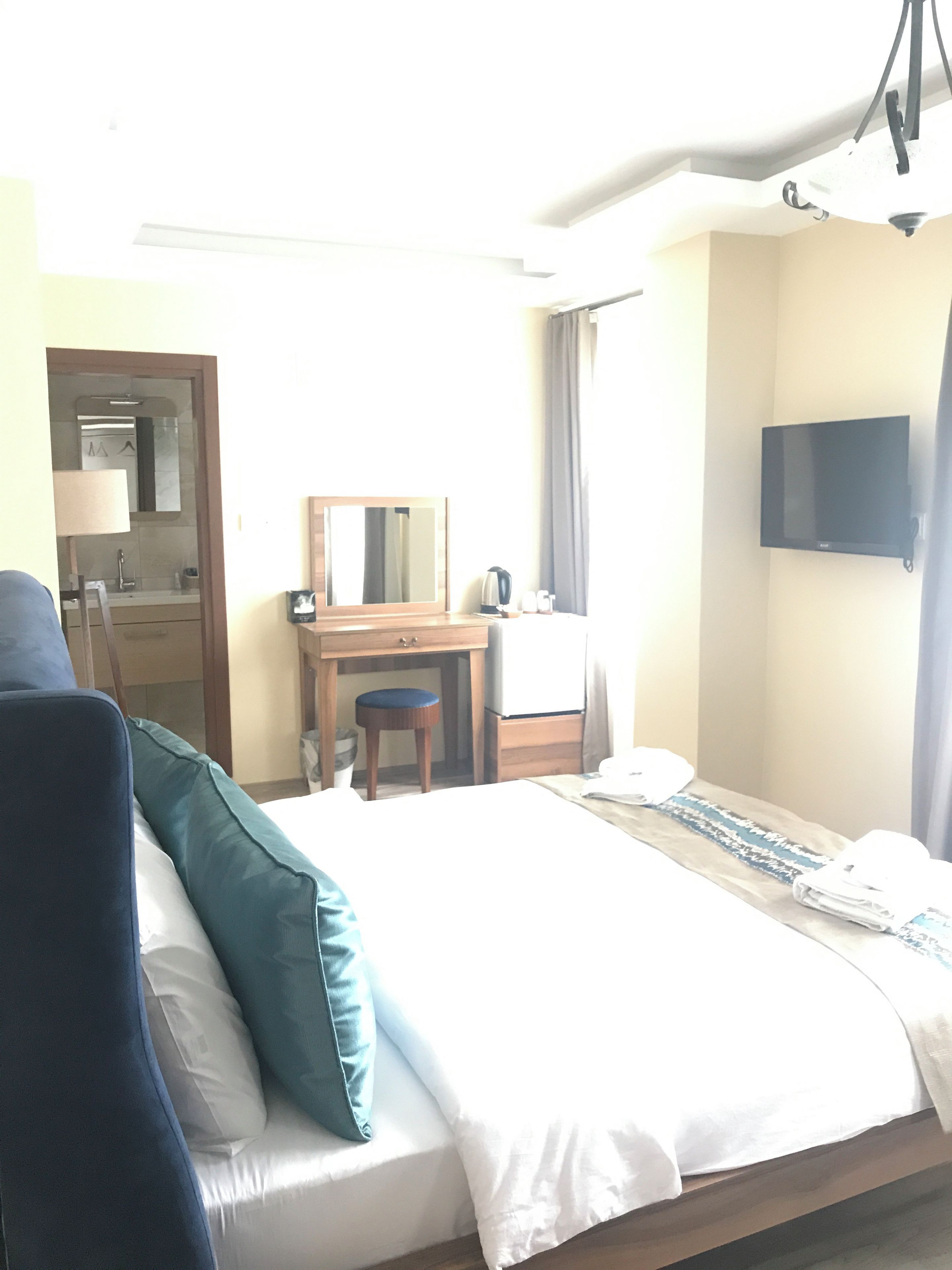 A hotel room with a bed, a desk, a chair, a television, and a bathroom visible through an open door.