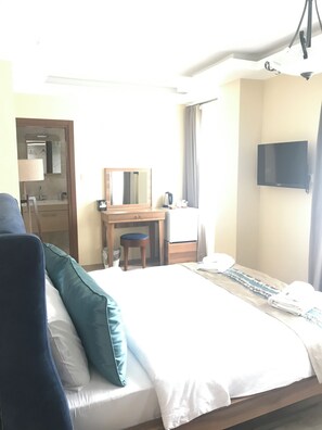 A hotel room with a bed, a desk, a chair, a television, and a bathroom visible through an open door.