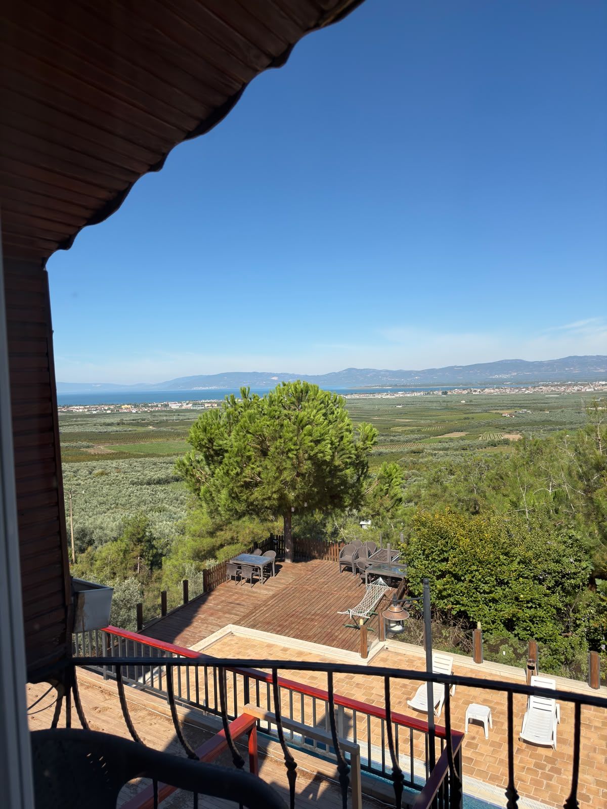 A balcony with a view of a coastal landscape, including a tree and a distant town.