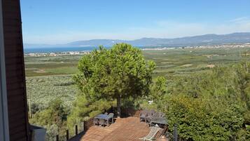 A balcony with a view of a coastal landscape, including a tree and a distant town.
