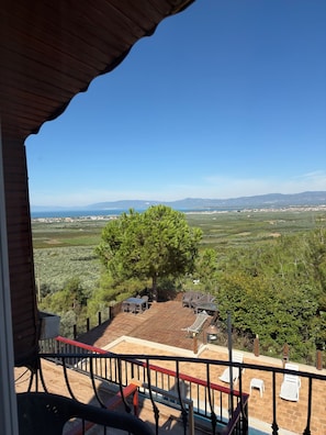 Un balcón con vistas a un paisaje costero, que incluye un árbol y un pueblo distante.