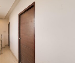 A closed wooden door with a metal handle, a white wall, and a tiled floor. - Classic Tj International (Lucknow)
