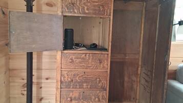 A wooden cabinet with drawers and a shelf, a black desk lamp, and a floor lamp against a wooden wall.