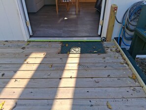 A wooden deck with a green mat at the entrance, a measuring tape, and a hose on the right.