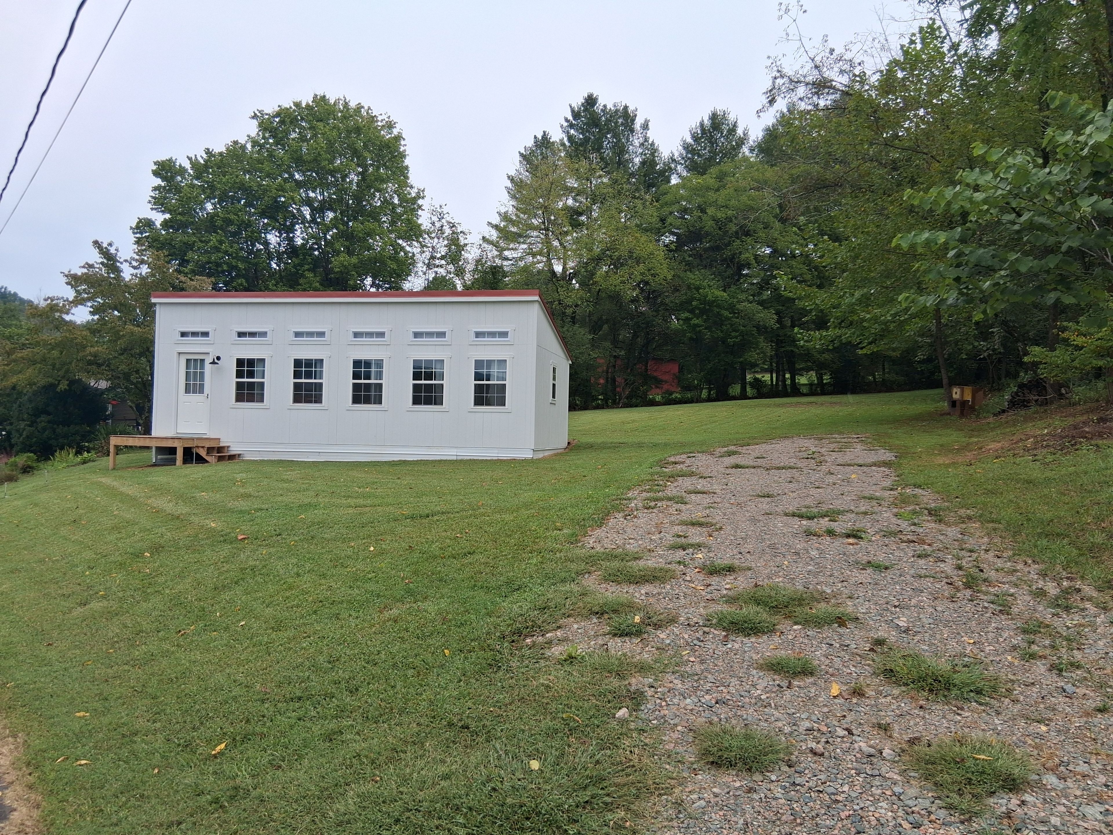 A white building with a red roof, surrounded by a grassy area and trees.