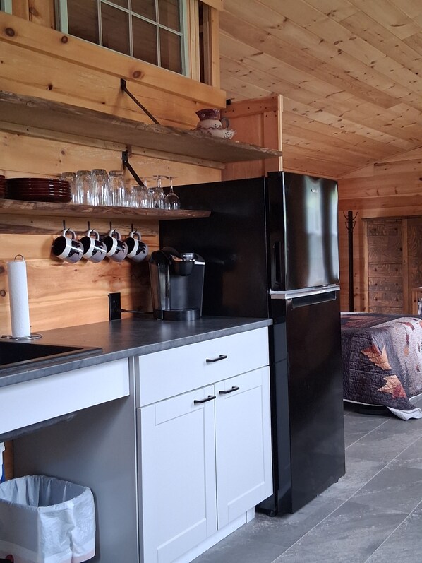 A compact kitchen with a black refrigerator, white cabinets, and a wooden ceiling.