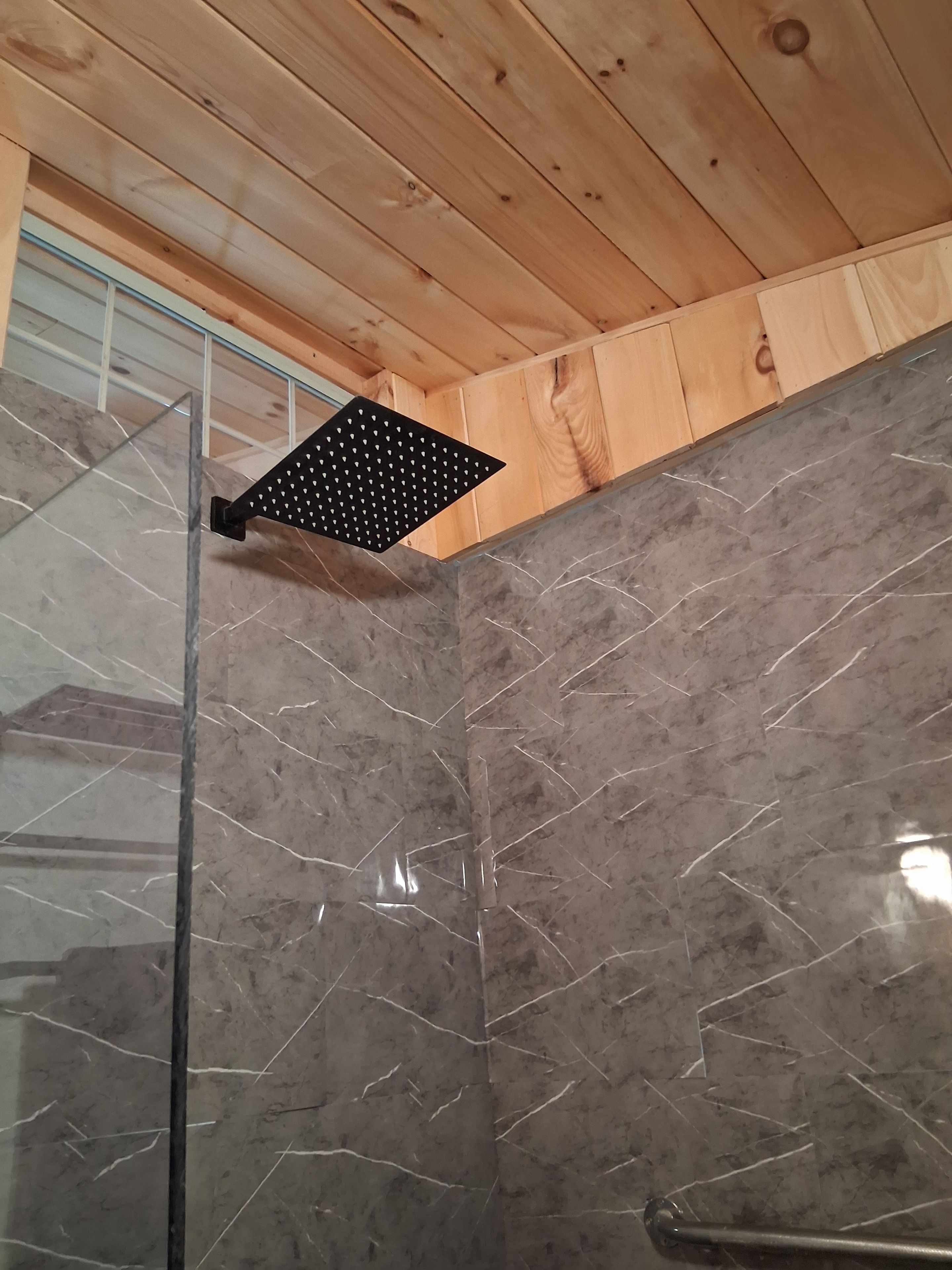 A corner of a room with a wooden ceiling, a glass shower enclosure, and a marble wall.