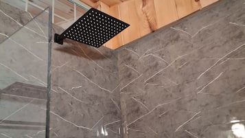 A corner of a room with a wooden ceiling, a glass shower enclosure, and a marble wall.