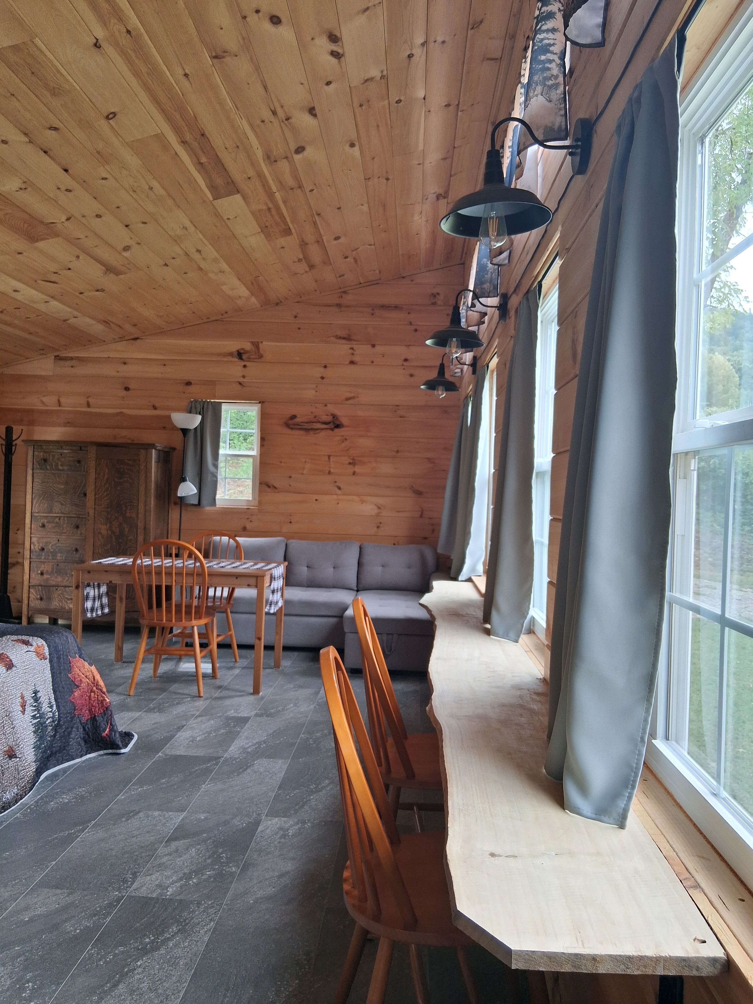 Een houten interieur met een bank, een eettafel, stoelen en een raam met gordijnen.