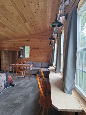 Un interior de madera con sofá, mesa de comedor, sillas y una ventana con cortinas.