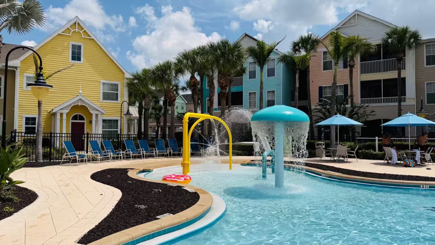 A swimming pool with a water feature, surrounded by lounge chairs and palm trees.