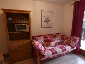 Ein Wohnzimmer mit einem Holzkabinett, einer Mikrowelle, einem rot-weißen Sofas und einem gerahmten Poster an der Wand.