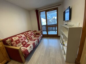 Een ingerichte kamer met een bank, een televisie aan de muur en uitzicht op besneeuwde bergen door een glazen deur.