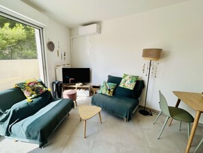 A modern living room with a sofa, a coffee table, a TV, and a dining area. - Air-conditioned apartment with terrace - 2 guests (Balaruc-les-Bains)