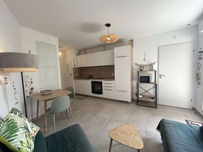 A compact kitchen with white cabinets, a microwave, and a dining area with a table and chairs. - Air-conditioned apartment with terrace - 2 guests (Balaruc-les-Bains)