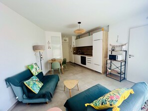 A compact living space with a kitchenette, a dining area, and a sofa with decorative pillows. - Air-conditioned apartment with terrace - 2 guests (Balaruc-les-Bains)