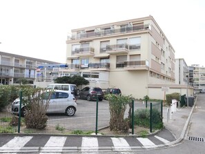 Ein mehrstöckiges Wohngebäude mit Balkonen, einem Parkplatz und einer Fußgängerüberweg.