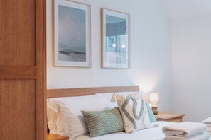 A hotel room with a bed, pillows, a nightstand, a lamp, and two framed pictures on the wall. - Halo Cottage by Navie Stays (Poole)
