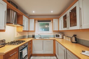 A modern kitchen with white cabinets, a stainless steel range hood, a built-in oven, a microwave, and a kettle. - Halo Cottage by Navie Stays (Poole)