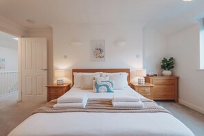 A neatly arranged bedroom with a large bed, two bedside tables, a wooden nightstand, a potted plant, and a wall-mounted artwork. - Halo Cottage by Navie Stays (Poole)