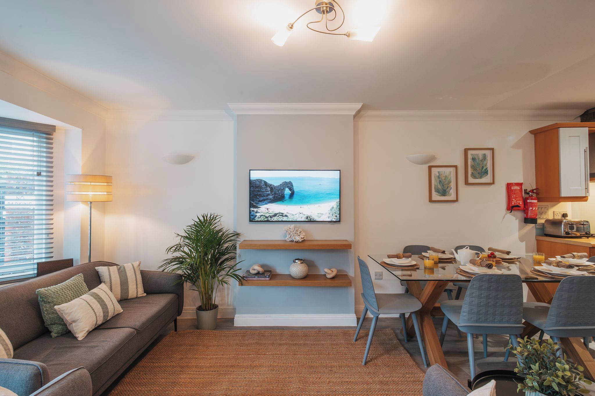 A living room with a sofa, a dining table set for two, and a television mounted on the wall.