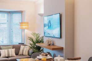A living room with a sofa, a lamp, a wall-mounted shelf with decorative items, and a framed picture. - Halo Cottage by Navie Stays (Poole)