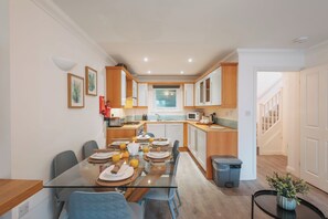 A modern kitchen with a dining area, wooden cabinets, and a glass table set for breakfast. - Halo Cottage by Navie Stays (Poole)