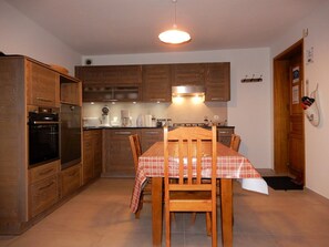 A compact kitchen with wooden cabinets, a dining table with chairs, and a built-in oven. - Apartment in chalet - 6 guests (Les Carroz d'Arâches)
