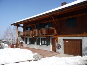 A two-story wooden building with a balcony, a garage, and a snow-covered ground. - Apartment in chalet - 6 guests (Les Carroz d'Arâches)