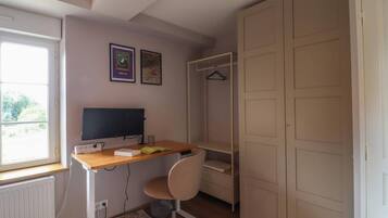 A bedroom with a bed, a desk with a computer, a chair, a wardrobe, and a window.