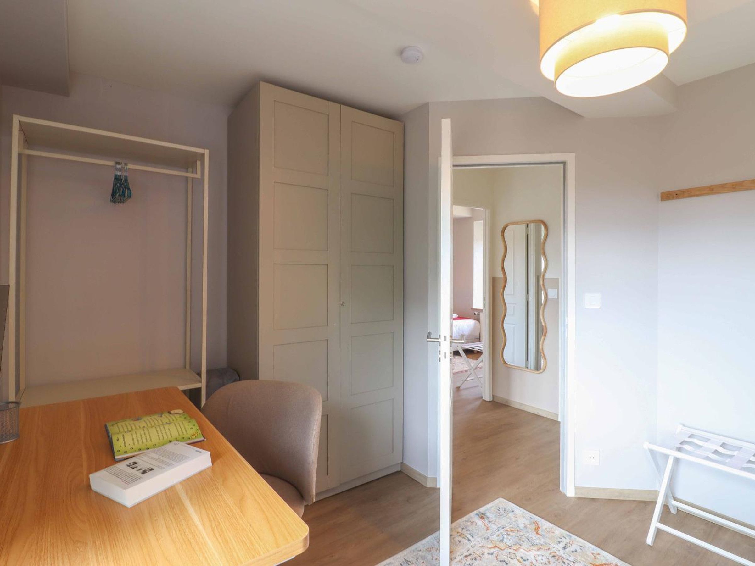 A room with a wooden dining table, a white chair, a wardrobe, and a mirror on the wall.