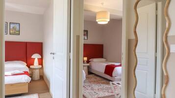 A hotel room with two beds, a red headboard, a bedside lamp, a mirror, and a hanging light fixture.